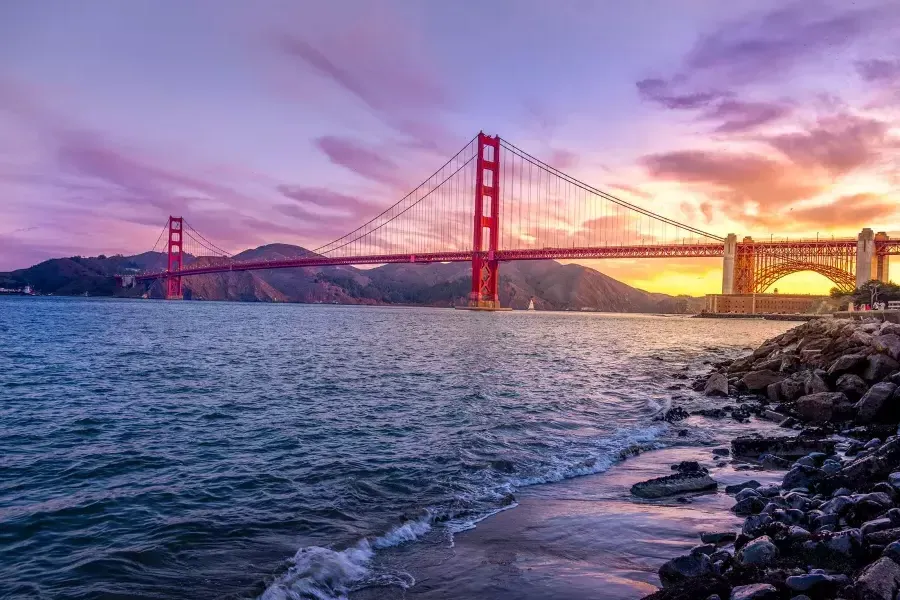 A Ponte Golden Gate ao pôr do sol 和 um céu multicolorido e a Baía de 威尼斯人官网平台app em primeiro plano.